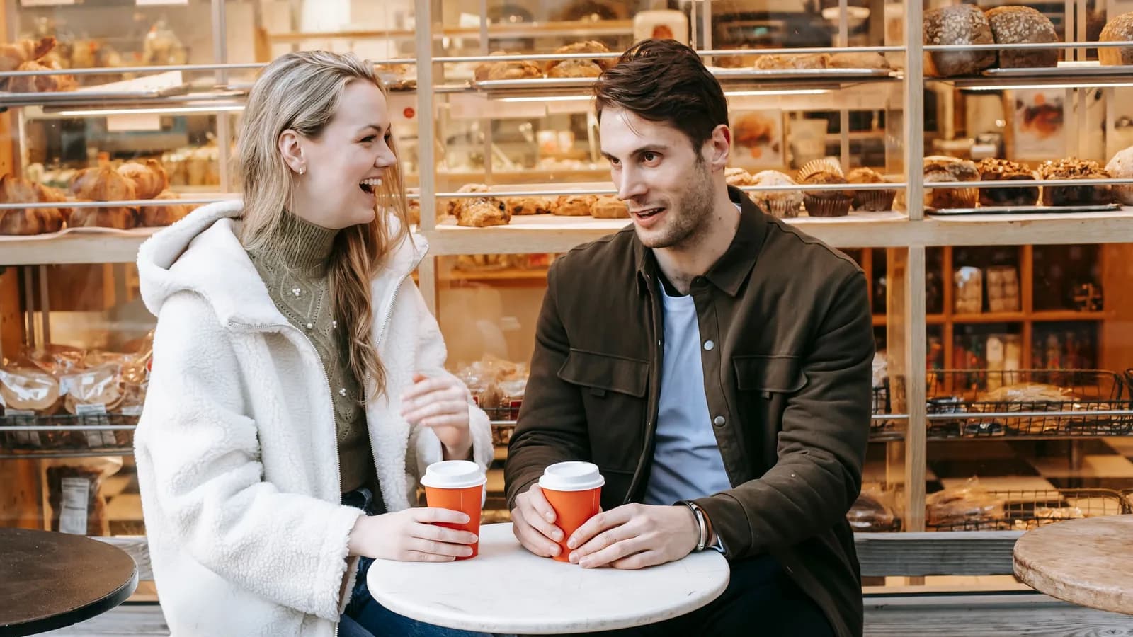 Eine Frau und ein Mann unterhalten sich lachend vor einer Bäckerei